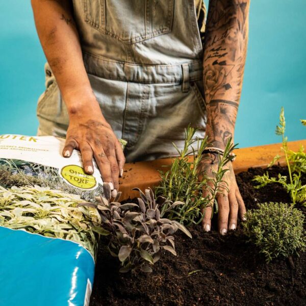 Una donna al lavoro su un'aiuola di erbe aromatiche con un sacchetto di terriccio biologico per erbe aromatiche di Terre Suisse