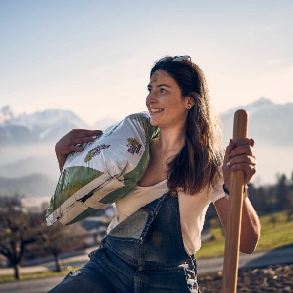 Une femme dans son jardin portant sur l'épaule un sac de terreau horticole de Terre Suisse.